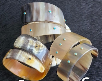 May include: A collection of horn bracelets in various shades of brown and tan. Each bracelet is adorned with small, turquoise-colored accents. The bracelets are labeled A, B, and C, and are displayed on a dark surface.