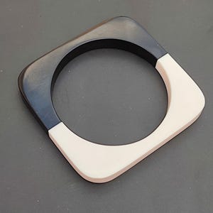 May include: A black and white square bangle bracelet. The bracelet is made of two halves, one black and one white, that are joined together to form a circle.