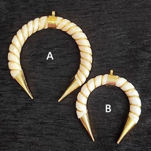 May include: Two crescent-shaped earrings. Each earring features a cream-colored, twisted design with gold wire accents. The ends are pointed and gold-colored. One earring is larger than the other. The background is black.