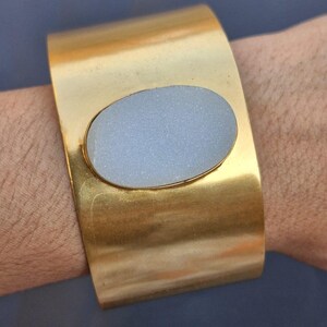 May include: A gold cuff bracelet with a large oval-shaped white stone set in the centre.