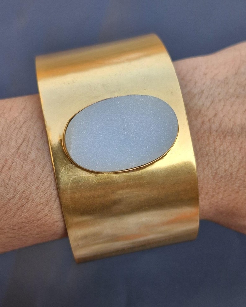May include: A gold cuff bracelet with a large oval-shaped white stone set in the centre.
