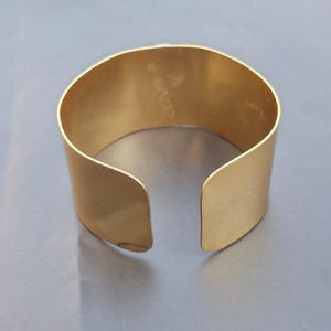 May include: A gold metal cuff bracelet with a smooth, polished finish. The bracelet is open on one side and has a slightly curved shape.