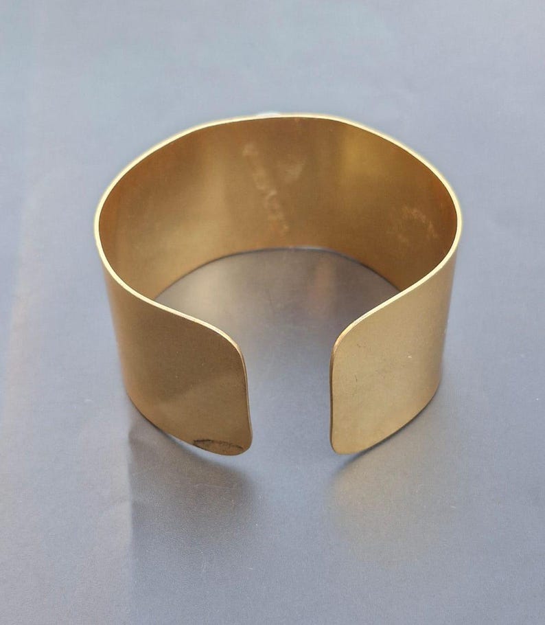 May include: A gold metal cuff bracelet with a smooth, polished finish. The bracelet is open on one side and has a slightly curved shape.
