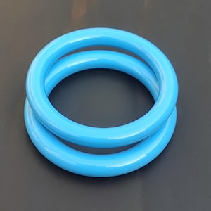 Może przedstawiać: Dwa jasnoniebieskie plastikowe bransoletki ułożone jedna na drugiej.