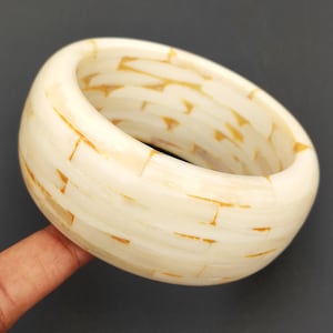 May include: A white bangle bracelet made of small, rectangular pieces of mother-of-pearl with a subtle golden shimmer.