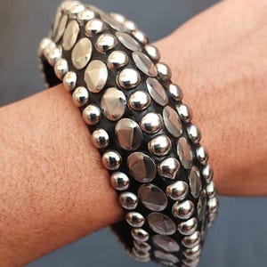 May include: A black leather bracelet with silver studs and round accents.