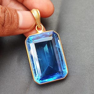 May include: A gold pendant featuring a large, rectangular, blue topaz gemstone.