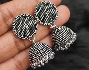 May include: A pair of silver earrings with a round, textured design. The earrings have a dangling, bell-shaped charm.