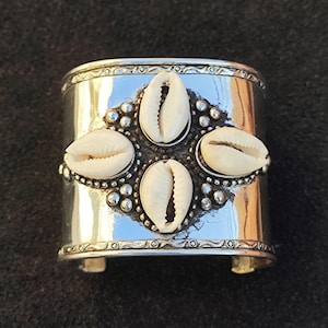 May include: Silver cuff bracelet with four white cowrie shells set in a silver design.