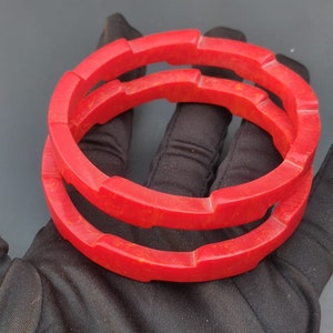 Puede incluir: Dos brazaletes de plástico rojo con un patrón de mármol. Los brazaletes están apilados uno encima del otro.