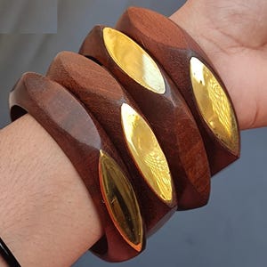 May include: Four brown wooden bangles with gold accents. The bangles are stacked on top of each other.