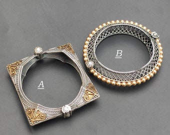 Puede incluir: Dos pulseras de plata con diseños intrincados. Una pulsera es de forma cuadrada con detalles dorados y la otra es redonda con cuentas doradas. Las pulseras están etiquetadas como A y B.