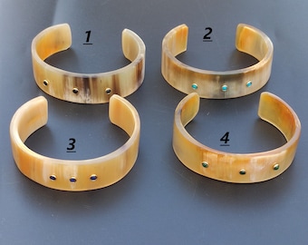 May include: Four horn bracelets with different colored stones. The bracelets are numbered 1 through 4.  Bracelet 1 has black stones, bracelet 2 has turquoise stones, bracelet 3 has blue stones, and bracelet 4 has green stones.