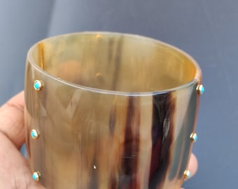 May include: A brown and black horn bangle bracelet with turquoise accents. The bracelet is made of natural horn and has a polished finish.