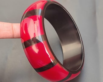 May include: A red and black striped bangle bracelet. The bangle is made of a glossy material and has a wide, flat design.