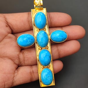 May include: Gold pendant in the shape of a cross with five oval turquoise stones.