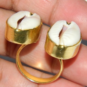 Op de afbeelding: Gouden ring met twee witte kauri schelpen. De ring is verstelbaar en heeft een eenvoudig ontwerp.