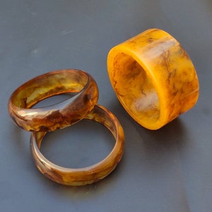 May include: Three brown and yellow patterned plastic bangles. The bangles are stacked on top of each other.