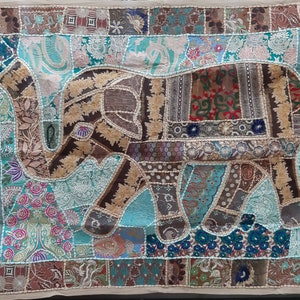 Puede incluir: Textil de patchwork con un diseño de elefante. El elefante es marrón y beige, con patrones intrincados. El fondo es una mezcla de parches turquesa, marrón y beige. El textil es rectangular y está enmarcado con un borde beige.