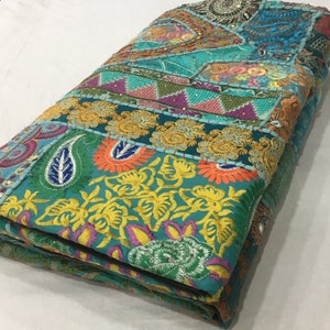 Pode incluir: Uma manta de patchwork azul turquesa com bordados e lantejoulas coloridas. A manta est&aacute; dobrada e tem uma variedade de padr&otilde;es florais e paisley.