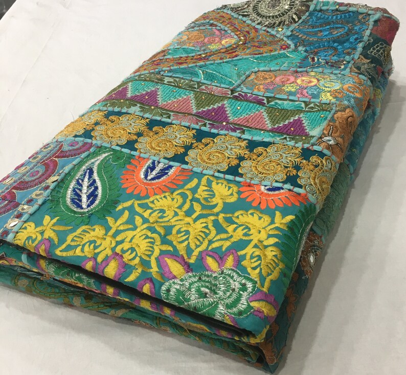 Pode incluir: Uma manta de patchwork azul turquesa com bordados e lantejoulas coloridas. A manta est&aacute; dobrada e tem uma variedade de padr&otilde;es florais e paisley.