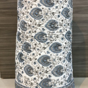 May include: A white cotton quilt with a blue and grey paisley pattern. The quilt is rolled up and has a border with a floral design.