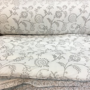 May include: A white cotton duvet cover with a grey floral print. The duvet cover is folded in half and the print is visible on both sides.