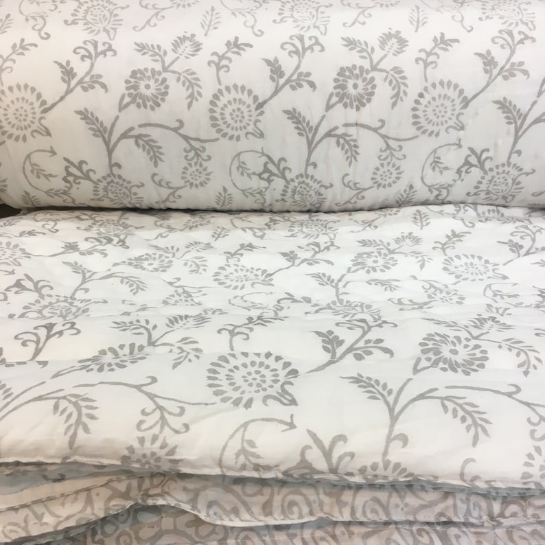 May include: A white cotton duvet cover with a grey floral print. The duvet cover is folded in half and the print is visible on both sides.