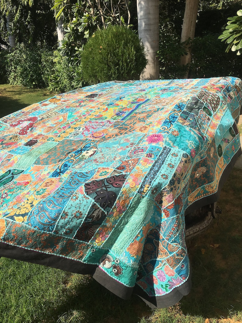 Pode incluir: Uma grande colcha de retalhos colorida com um fundo turquesa. A colcha &eacute; feita de v&aacute;rios tecidos e &eacute; decorada com bordados e lantejoulas.