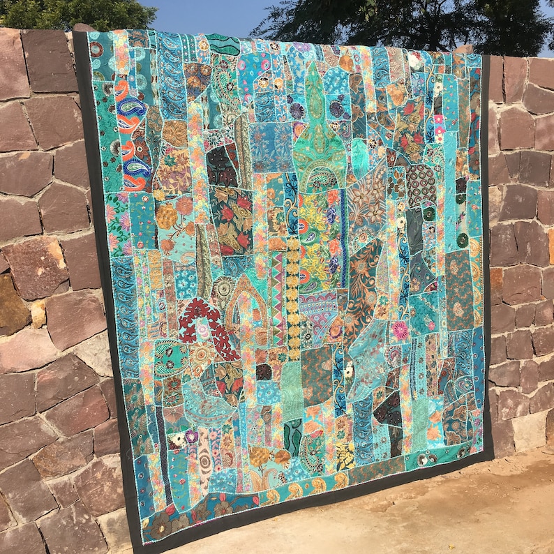 Pode incluir: Uma colcha de retalhos grande e colorida com uma variedade de tecidos e padr&otilde;es em tons de azul, verde e marrom. A colcha &eacute; composta por muitos quadrados e ret&acirc;ngulos pequenos, cada um com um design diferente. A colcha &eacute; bordada com uma bainha preta.
