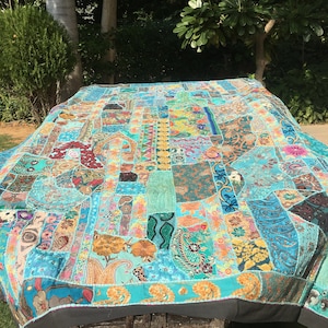 Pode incluir: Uma grande colcha de retalhos colorida com um fundo turquesa. A colcha &eacute; feita de v&aacute;rios tecidos e padr&otilde;es, incluindo padr&otilde;es paisley, florais e geom&eacute;tricos. A colcha &eacute; bordada com contas e lantejoulas.