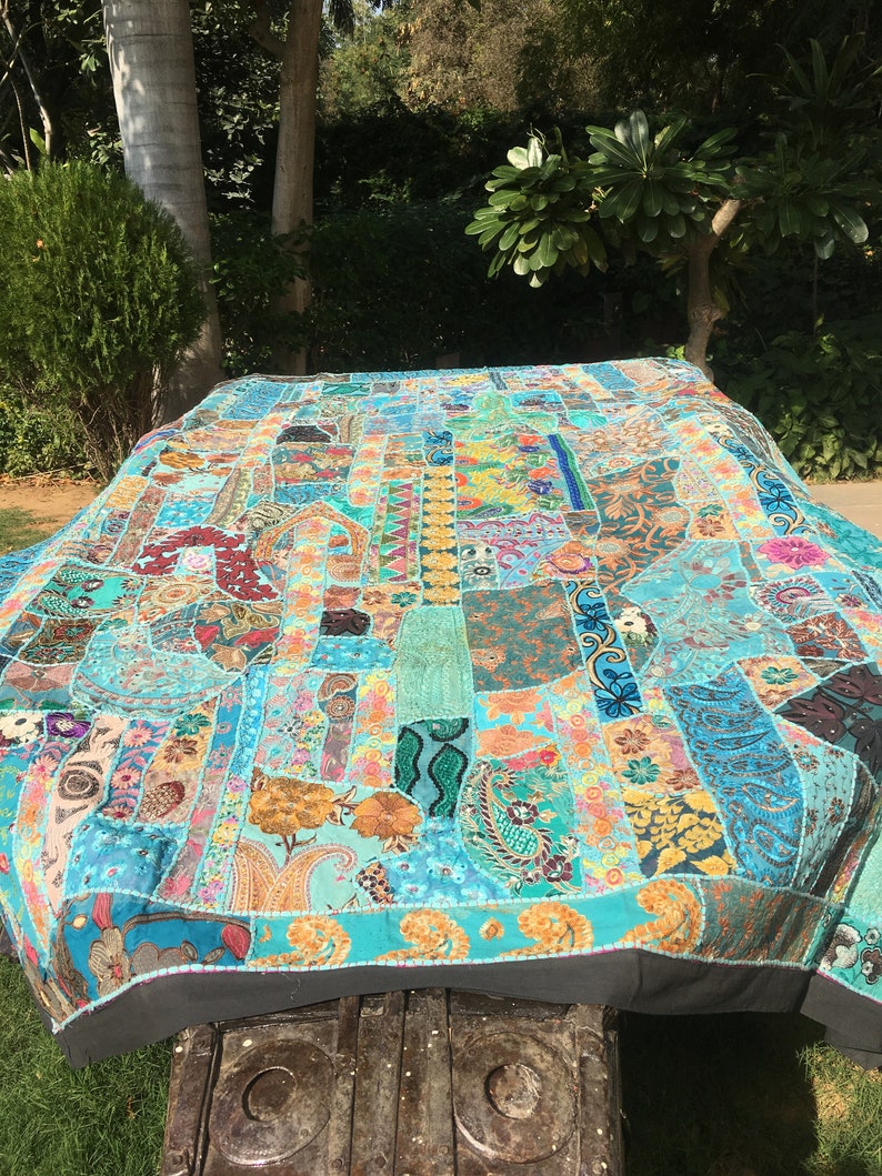 Pode incluir: Uma grande colcha de retalhos colorida com um fundo turquesa. A colcha &eacute; feita de v&aacute;rios tecidos e padr&otilde;es, incluindo padr&otilde;es paisley, florais e geom&eacute;tricos. A colcha &eacute; bordada com contas e lantejoulas.