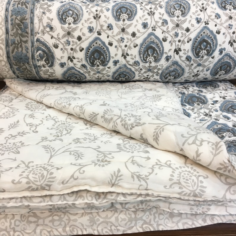 May include: A white and blue patterned quilt with a floral design. The quilt is folded in half and the top layer is folded back to reveal the white fabric underneath.