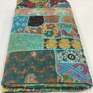 Pode incluir: Uma colcha de retalhos azul turquesa com v&aacute;rios padr&otilde;es florais bordados e detalhes coloridos. A colcha &eacute; feita de diferentes tecidos e texturas, criando um estilo &uacute;nico e bo&eacute;mio.