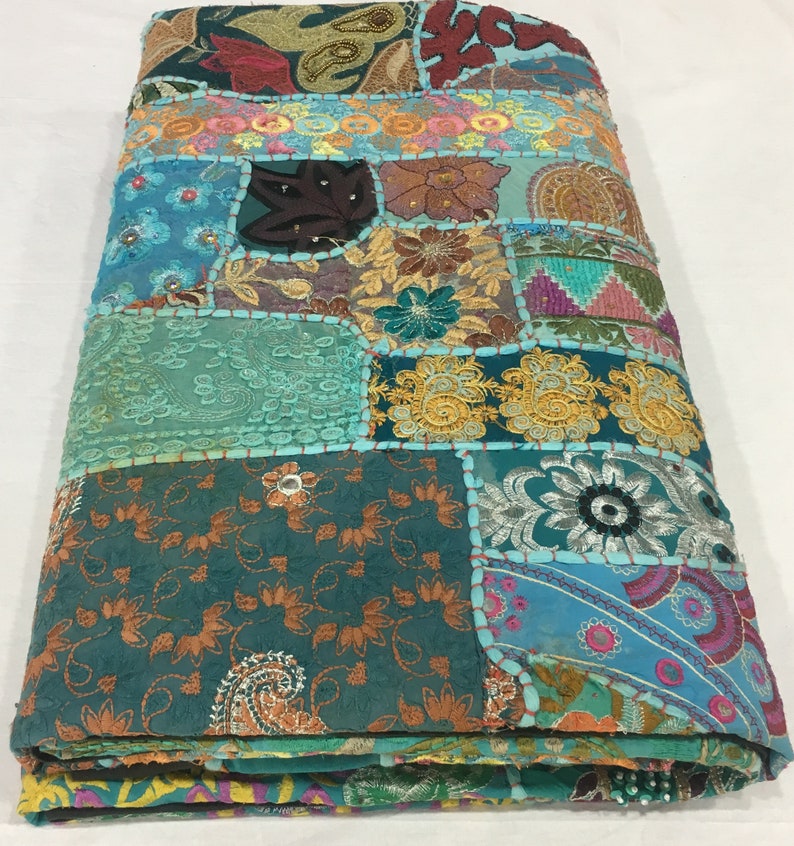 Pode incluir: Uma colcha de retalhos azul turquesa com v&aacute;rios padr&otilde;es florais bordados e detalhes coloridos. A colcha &eacute; feita de diferentes tecidos e texturas, criando um estilo &uacute;nico e bo&eacute;mio.