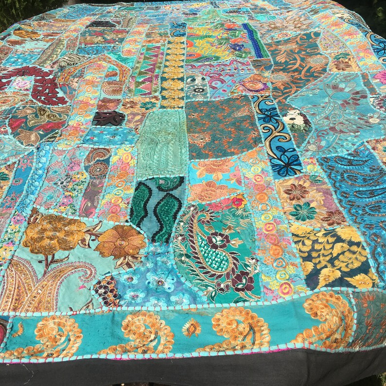 Pode incluir: Uma colcha de retalhos grande e colorida com um fundo turquesa. A colcha &eacute; feita de v&aacute;rios tecidos e padr&otilde;es, incluindo desenhos paisley, florais e geom&eacute;tricos. A colcha &eacute; decorada com lantejoulas e bordados.