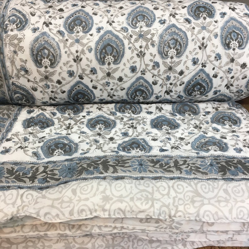 May include: A white cotton quilt with a blue and grey floral pattern. The quilt is folded in half and the pattern is visible on both sides.
