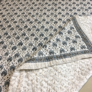 May include: A white cotton quilt with a blue and brown paisley print. The quilt is folded in half, showing the back side, which has a smaller floral print.