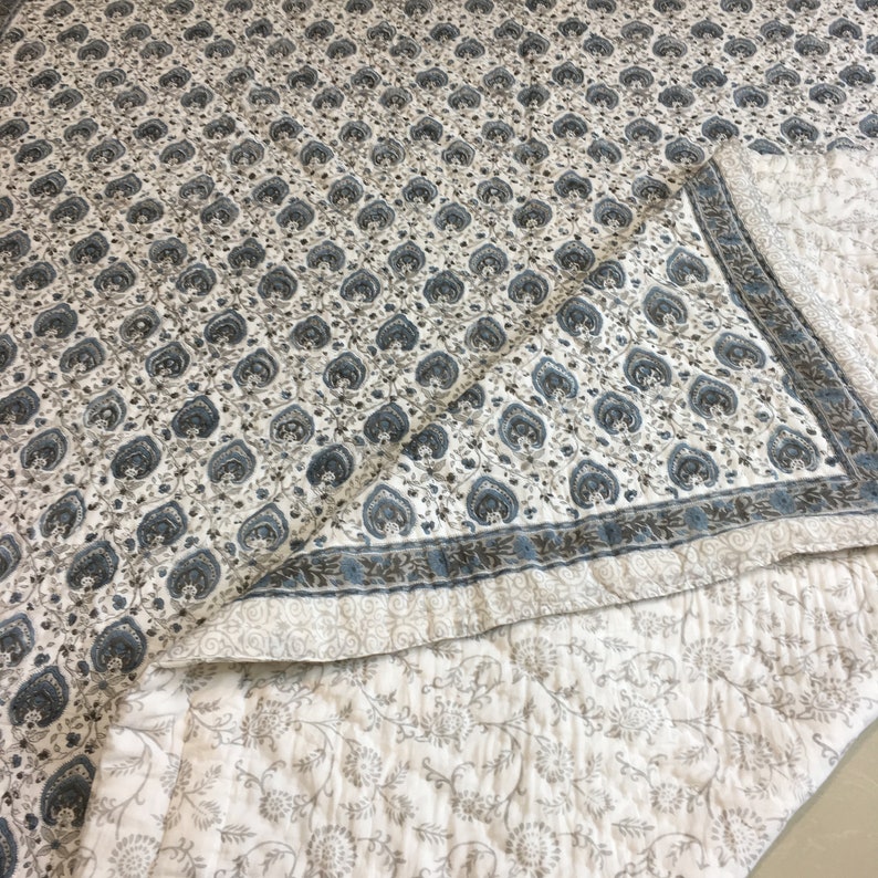 May include: A white cotton quilt with a blue and brown paisley print. The quilt is folded in half, showing the back side, which has a smaller floral print.