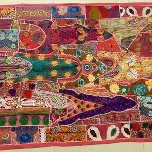 May include: A colourful patchwork wall hanging with embroidered floral designs. The fabric is a mix of pink, green, blue, yellow, and red. The hanging is made up of many different pieces of fabric sewn together.