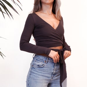 May include: A woman wearing a dark gray long-sleeved wrap top with a tie at the waist and light blue jeans.