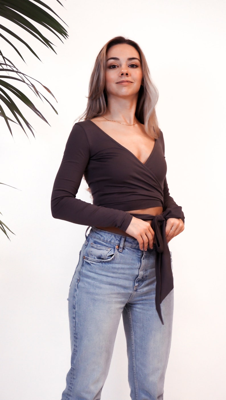May include: A woman wearing a dark gray long-sleeved wrap top with a tie at the waist and light blue jeans.