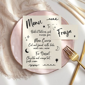 May include: A pink plate with a white menu card on top. The menu card has a handwritten menu with the text "Menu", "To Start", "Beetroot Tartlets, goat mousse, pom", "Main Course", "Cod and fennel risotto, kale, cavolo nero, sauce", "For Dessert", "Chocolate and orange tart, fresh cream". A white card with the text "Freyja" is placed on the plate. A gold fork and knife are placed on the plate.
