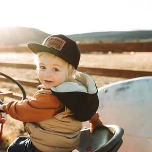 May include: A black baseball cap featuring a rectangular brown patch on the front with the text Blame Roots. The cap has a flat brim and is constructed from a solid black fabric, providing a structured look with clear, legible lettering.