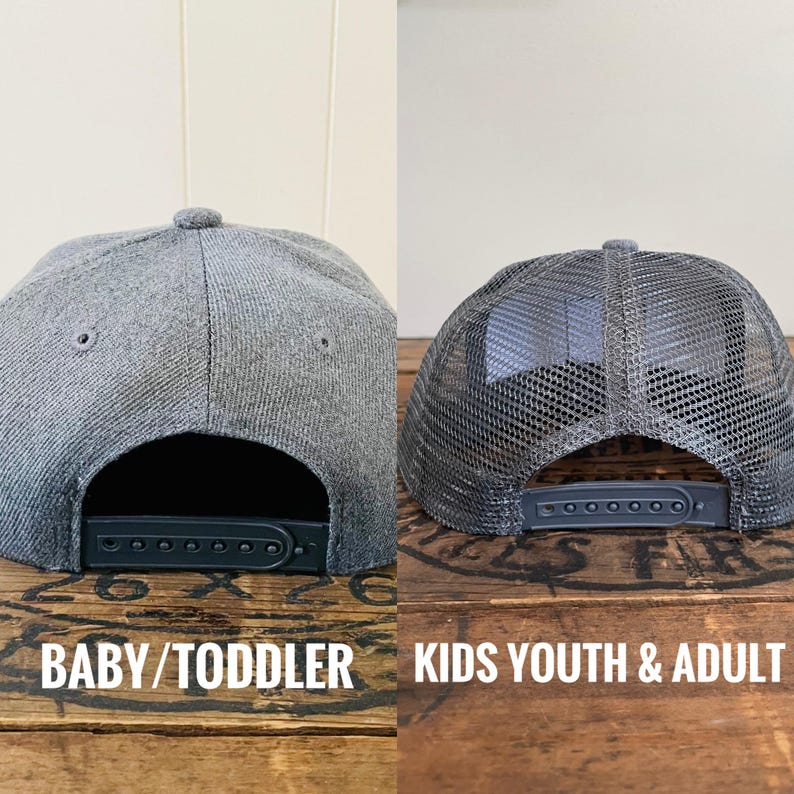 May include: Two grey baseball caps shown from the back. The left cap is a solid grey fabric with a plastic snapback closure labelled BABY/TODDLER. The right cap features a grey mesh back panel and a plastic snapback closure labelled KIDS YOUTH & ADULT.