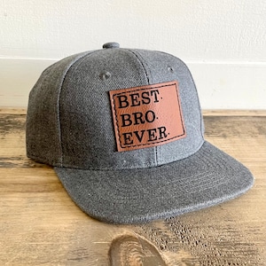 Puede incluir: Una gorra de béisbol gris con un parche de cuero marrón que dice "BEST BRO. EVER."