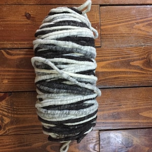 May include: A skein of thick, chunky yarn in black and white. The yarn is made of wool and is perfect for knitting or crocheting.