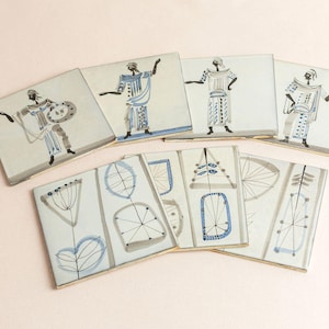 May include: Set of eight ceramic tiles with a white background and blue and grey designs. Some tiles feature stylised figures, while others feature abstract patterns.