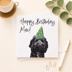 May include: A square white greeting card featuring a black illustration of a fluffy dog wearing a teal party hat with yellow polka dots. The text "Happy Birthday Max!" is printed in black script above the dog's head on the front of the card.
