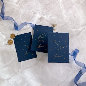 May include: Three blue cards with gold foil constellation illustrations and names. The constellations are Aries, Aquarius, and Pisces.